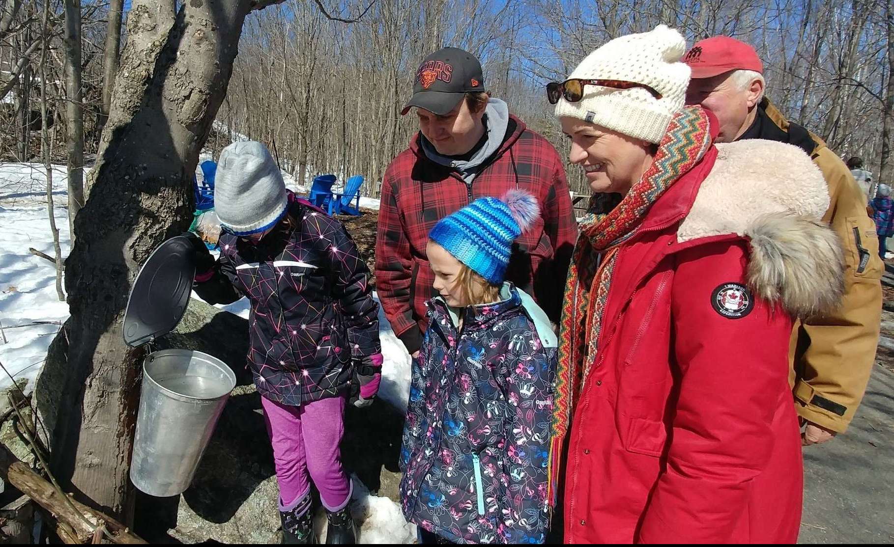 Family at Maple Sugar Shack looking at sap collection buckets on maple tree