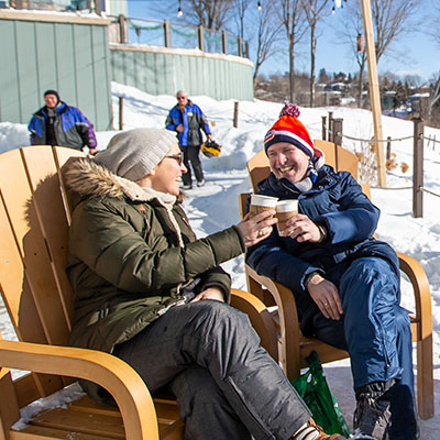 Two people sitting on a patio in winter cheersing their cups