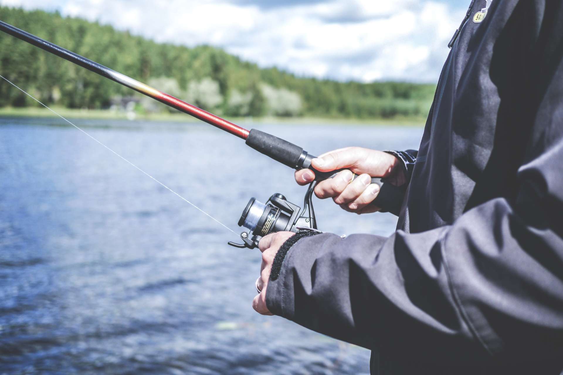 Man reeling in fishing rod with lake background
