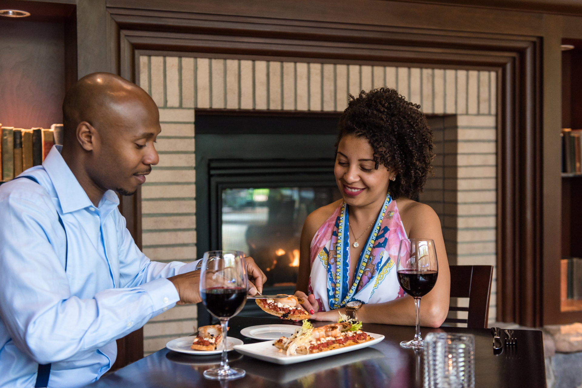 A couple in front of a fireplace with wine and food