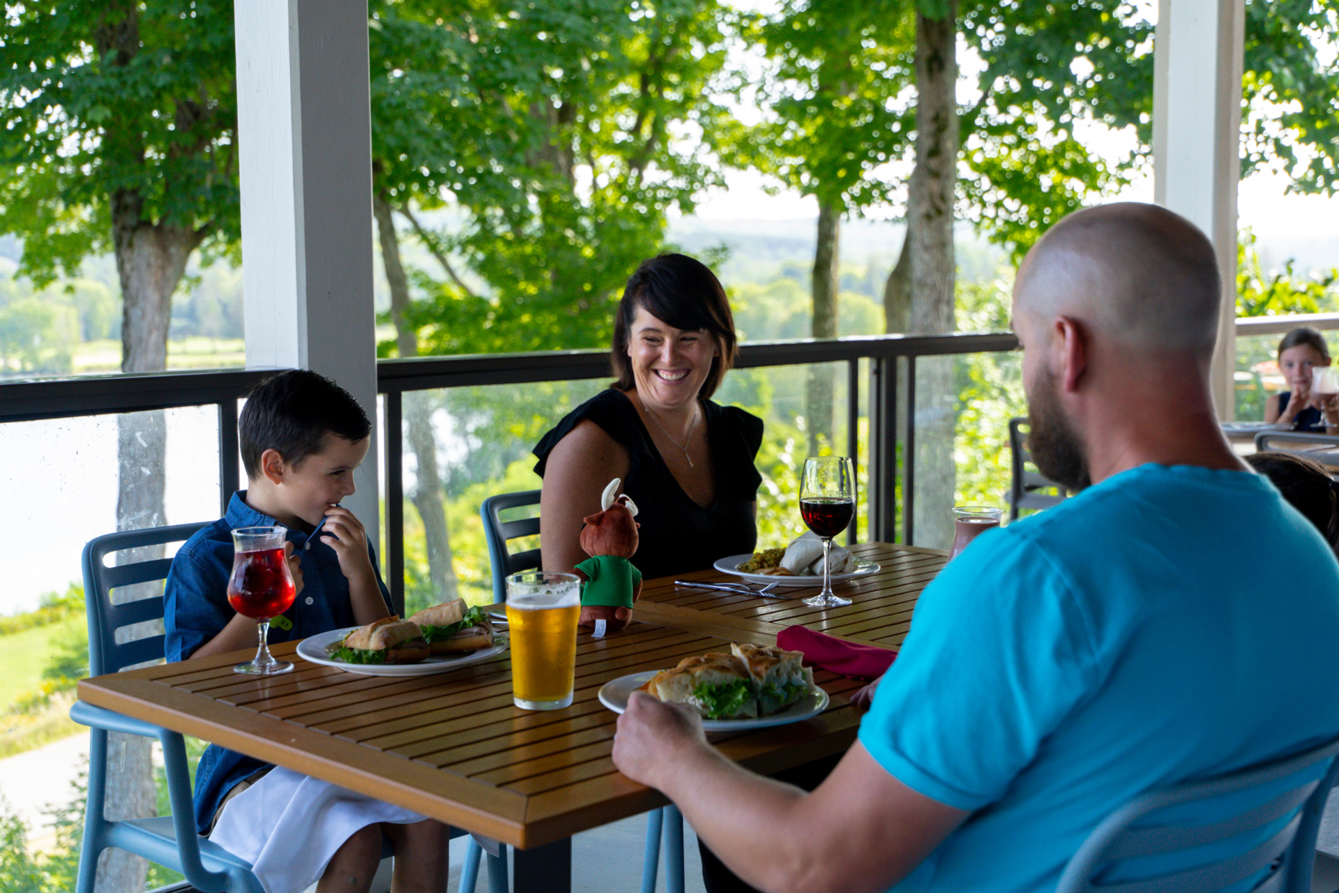 Family of three sitting on a patio table with trees in the distance