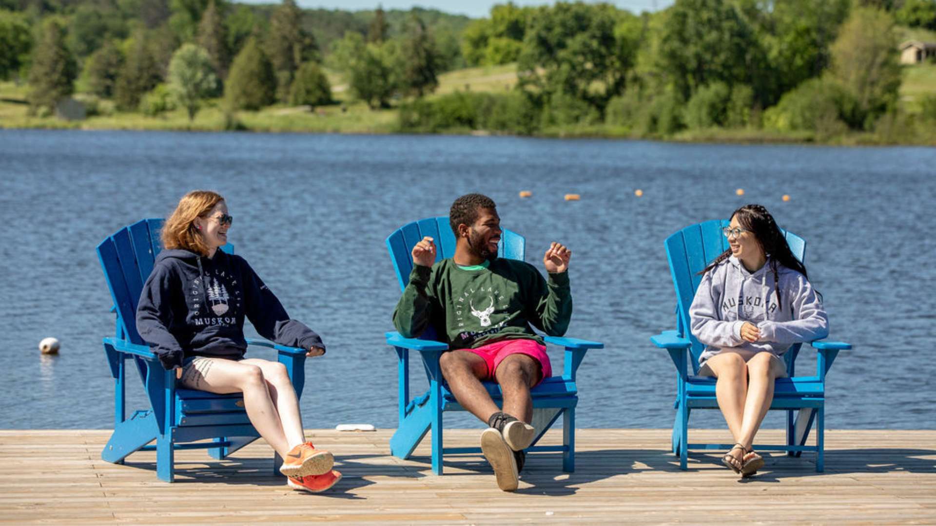 Three staff members sitting on a dock in muskoka chairs