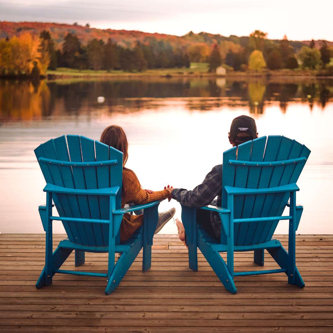 A couple sitting side by side in muskoka chairs looking at the lake