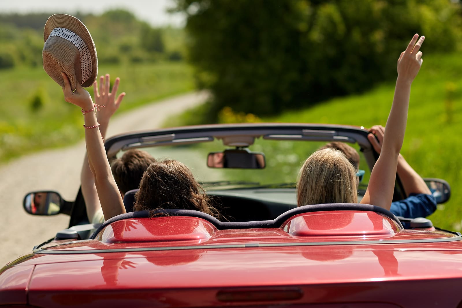 eisure, road trip, travel and people concept - happy friends driving in cabriolet car at country and waving hands